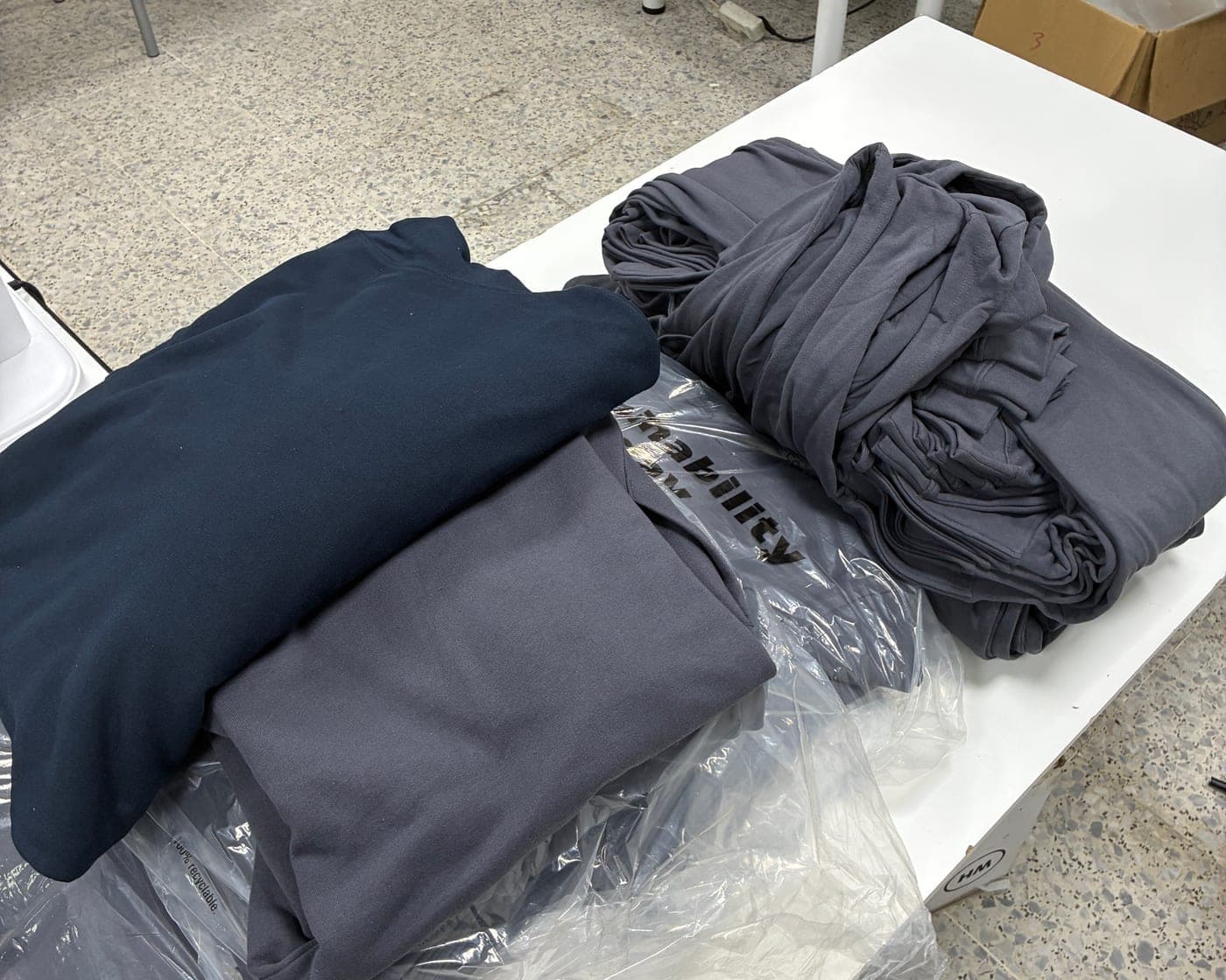 Sudaderas azul marino y gris dobladas sobre una mesa del taller antes de estamparlas, con el tejido de felpa a la vista