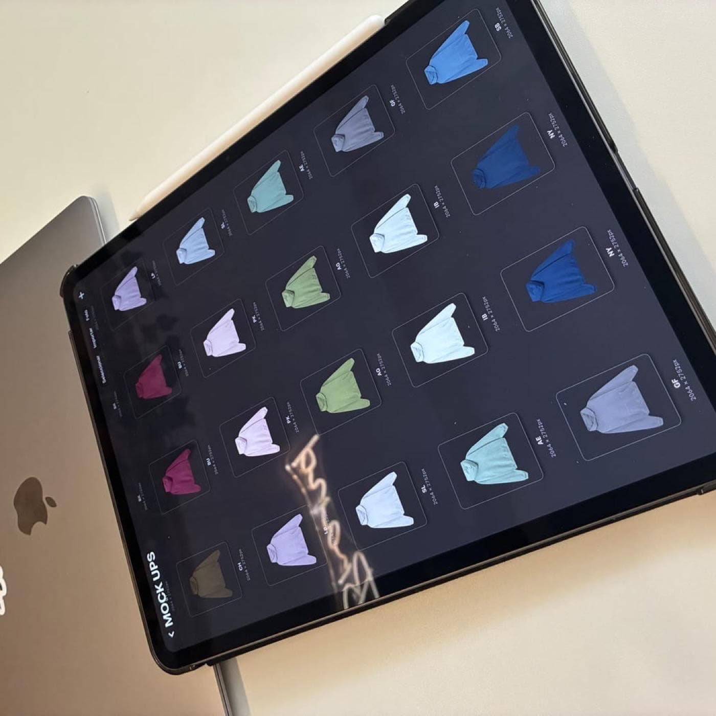 Tableta sobre una mesa mostrando una cuadrícula de mockups de sudaderas en distintos colores durante la fase de diseño