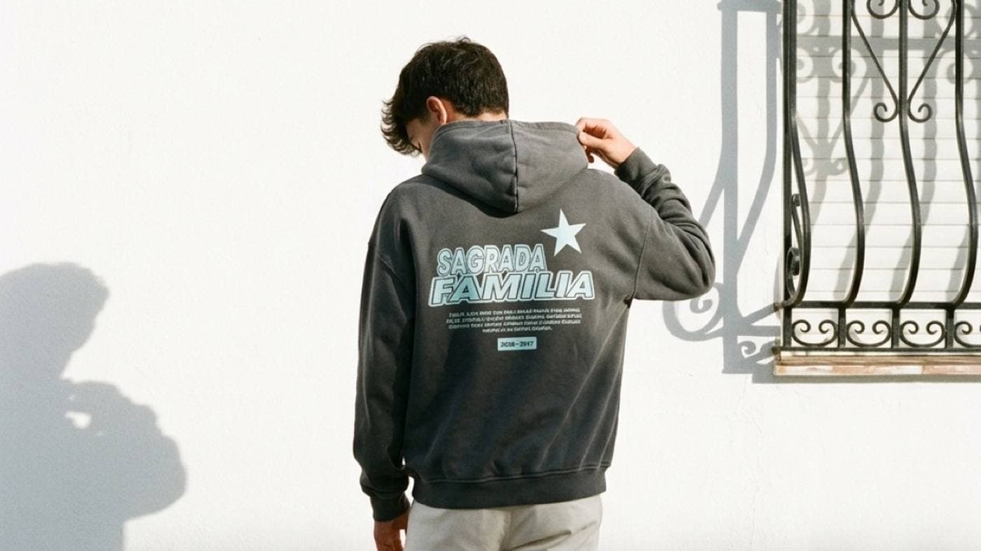 Chico de espaldas junto a una reja andaluza con una sudadera gris que pone Sagrada Familia con una estrella